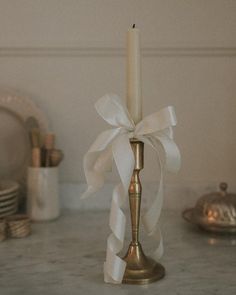 a gold candle holder with a white ribbon tied around it on a marble countertop