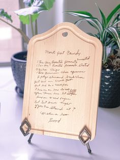 a wooden plaque with writing on it sitting next to a potted plant in front of a window