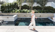 a person walking in front of a pool with water and plants on the other side