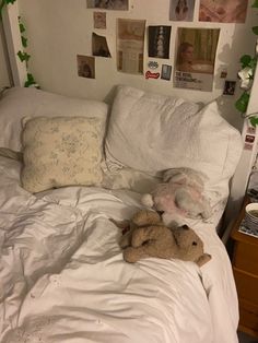 a bed with white sheets and stuffed animals on top of it, surrounded by photos