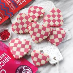 pink and white checkered cookies are on the counter next to some red powdered sugar