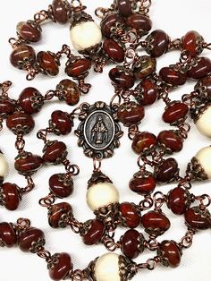 This five decade Catholic Rosary is made with 53 beautiful 8 mm Wine Color Poppy Jasper Rondelle beads, and 6 larger (10 mm) Cream Color Riverstone Beads (as the Our Father Beads). There are a total of 130 copper bead caps layered on the beads. This rosary is considered unbreakable due to the wire wrapping technique I use (not a simple loop, but wrapped around 3 times). The crucifix is a 2 Inch copper Crucifix, and is beautifully detailed. The center is a copper Miraculous Medal. JASPER: a semi- Handmade Artisan Rosary, Artisan Handmade Rosary, Artisan Brown Oval Beads, Gems, And Cabochons, Poppy Jewelry, Rosary Prayers Catholic, Protestant Prayer Beads, Chaplet Rosary, Poppy Jasper, Art Deco Jewelry Vintage