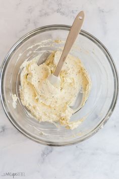 a glass bowl filled with batter on top of a white marble countertop next to a wooden spoon