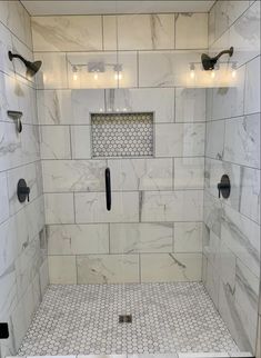 a walk in shower with white marble tile and black handles on the door, along with two lights