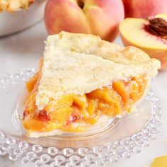 a piece of pie sitting on top of a glass plate next to some peaches