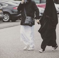 two women walking down the street while talking on their cell phones and one is wearing a hijab