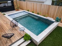 an above ground swimming pool surrounded by wooden decking and lawn area with two chairs