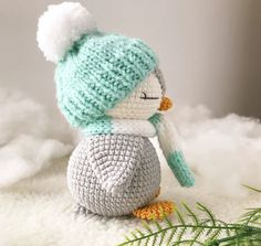 a crocheted penguin sitting on top of a fluffy white blanket next to a plant