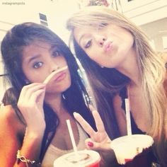 two young women sitting next to each other at a table with drinks in front of them