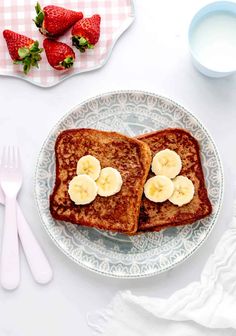 two slices of french toast on a plate with bananas and strawberries next to it