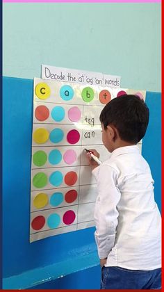 a young boy writing on a bulletin board with colorful circles and words written on it