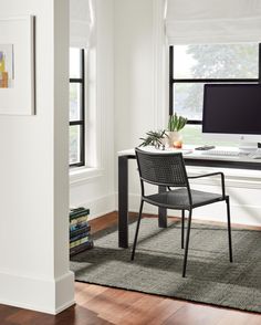 a desk with a computer on top of it in front of two windows and a rug