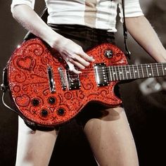 a woman is holding a red guitar in her right hand and wearing short black shorts