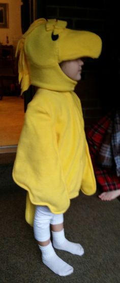 a child in a yellow dinosaur costume standing on the floor next to a man wearing white socks