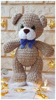 a crocheted teddy bear with a blue bow tie and gold stars around it