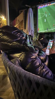 two people sitting on a couch in front of a large screen tv with soccer playing on it