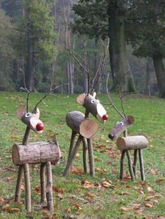 three wooden reindeer statues sitting on top of a lush green field with trees in the background