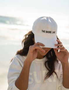 The logo baseball hat is a cotton hat that features an adjustable back strap. The embroidered THE SHORE LINE logo in contrast stitching sits at the center front. Size - one size fits most Beach Merch Photoshoot, Photos With Hats, Women In Baseball Hats, Hat Product Photography, Hat Photoshoot Ideas, Merch Photoshoot Ideas, Hat Ads, Hat Modeling, Clothing Poses