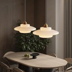 two lights hanging over a table with chairs and a potted plant in the corner