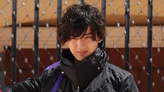 a young man in black jacket standing next to a fence and holding a red frisbee