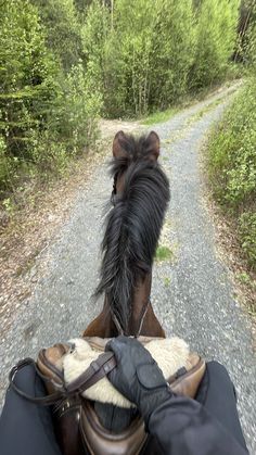 a person riding on the back of a brown horse down a dirt road with trees in the background