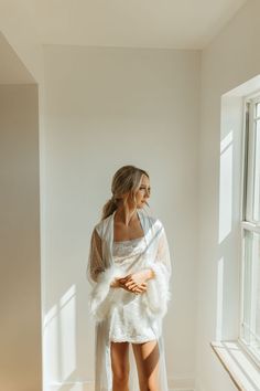 a woman standing in front of a window wearing a white dress with feathers on it