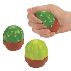 a hand is holding two green and red plastic cactus pots, one with yellow stars on it