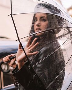 a woman holding an umbrella while standing in front of a car on a rainy day