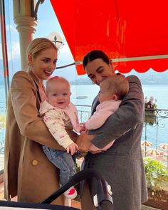 two women and a baby are standing under an umbrella by the water with their arms around each other