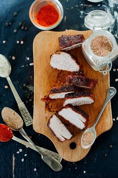 slices of meat sitting on top of a cutting board next to spices and spoons