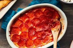 a pepperoni pizza in a white casserole dish with a wooden spoon next to it