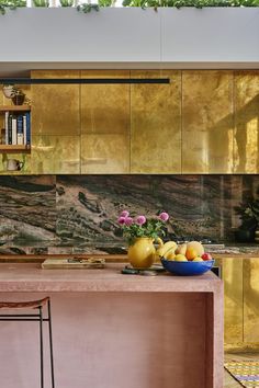 a bowl of fruit is on the kitchen counter next to a vase with flowers in it