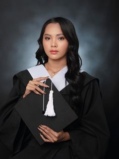 a woman wearing a graduation gown and holding a black square with white tassels