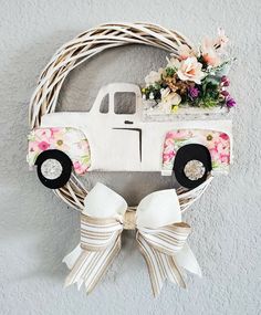 a wreath with a white truck and flowers hanging on the side of a wall next to a bow