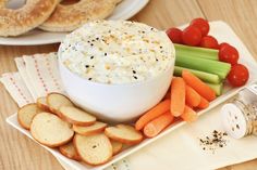 a bowl of dip surrounded by carrots, celery and crackers