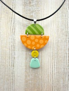 an orange, green and yellow necklace with polka dots on the bottom is hanging from a black cord