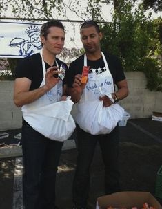 two men standing next to each other holding bags of food and bottles in their hands