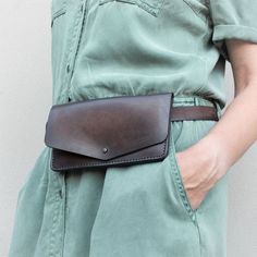 a woman wearing a green dress and holding a brown leather belt bag in her right hand