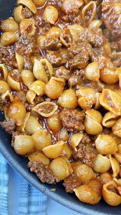 pasta with meat and sauce in a skillet on a blue towel next to a spoon