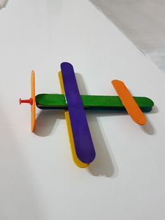 an airplane made out of pops sticks on top of a white surface with one plane sticking out of it's side