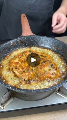 a frying pan filled with food sitting on top of a stove next to a person