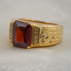 a gold ring with a large red stone surrounded by small white diamonds on a plain surface