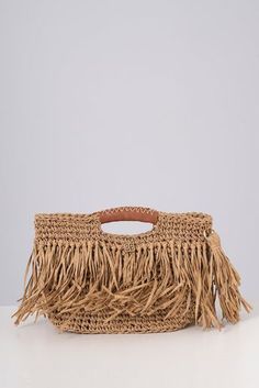 a straw bag with fringes on the handle and handles, sitting on a white surface