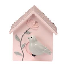 a white bird sitting on top of a pink house shaped clock with flowers and leaves