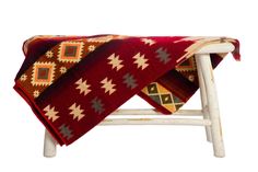 a red and yellow blanket sitting on top of a wooden chair next to a white wall