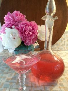 two glasses filled with liquid sitting on top of a table next to pink and white flowers