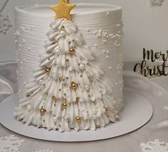 a white christmas cake with gold decorations and a star on top, sitting on a table