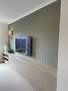 a flat screen tv sitting on top of a wooden shelf in a living room next to a window