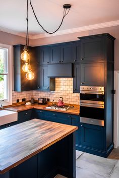 a kitchen with blue cabinets and wooden counter tops, lights hanging from the ceiling over the stove