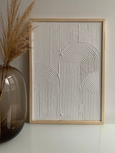 a vase with some dry grass in it next to a framed art piece on a shelf